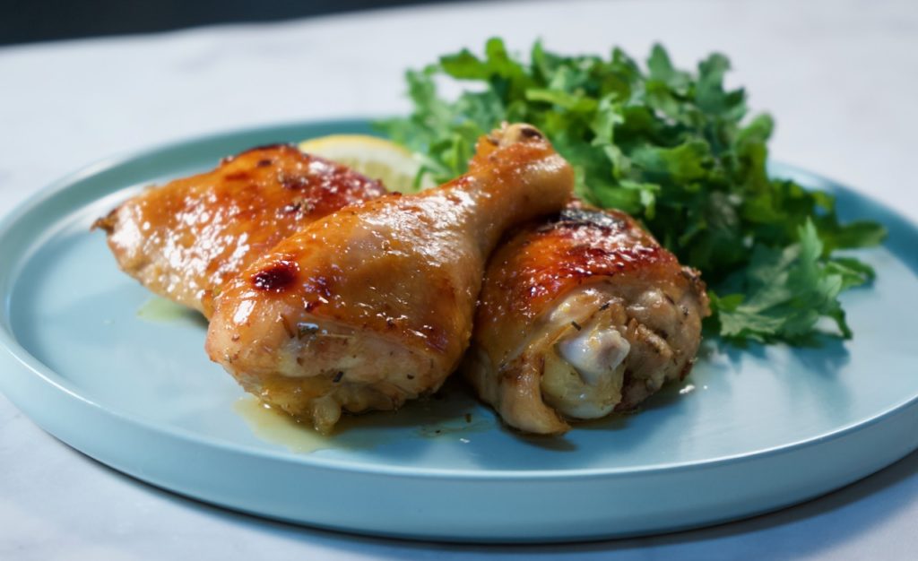 Roasted chicken pieces on a plate with greens and lemon.