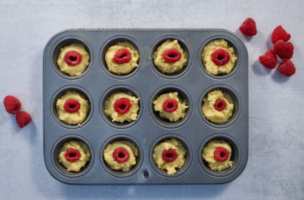 Madeleine batter in a mini muffin tin with raspberries.