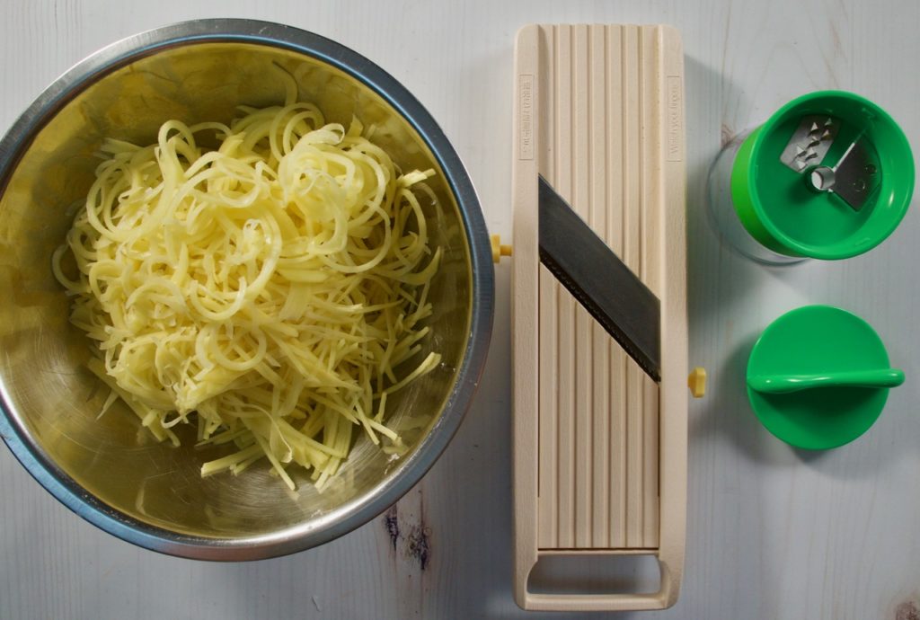 Tartiflette potato julienned. Mandoline and spiralizer shown as tools.