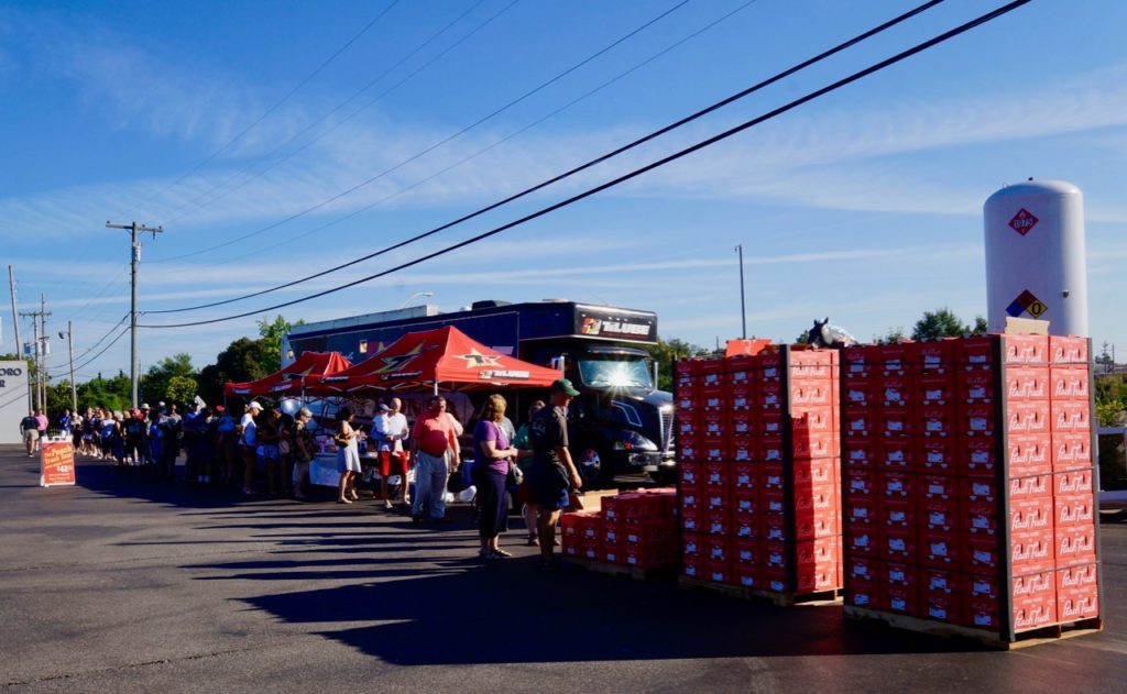 People waiting in line for peaches. Stacks of pallets of fresh peaches waiting to be sold.