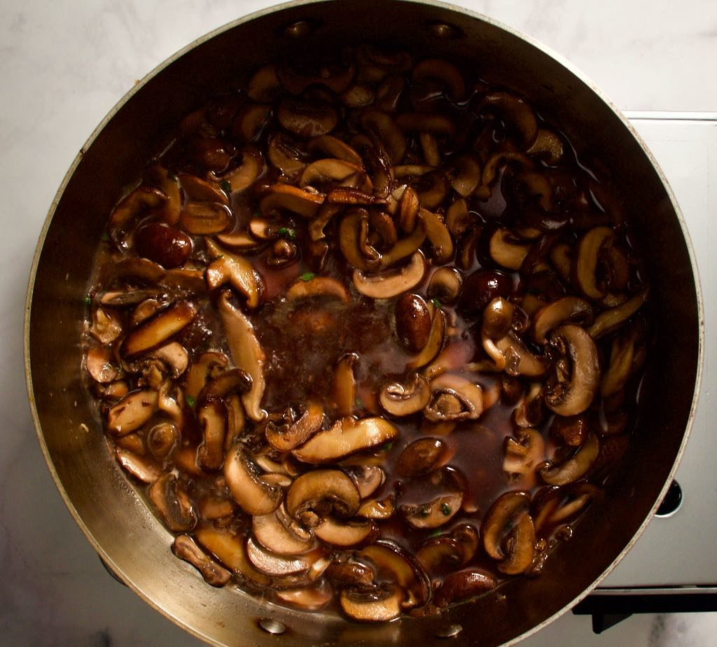 Mushrooms simmering in a pan with red wine and stock.