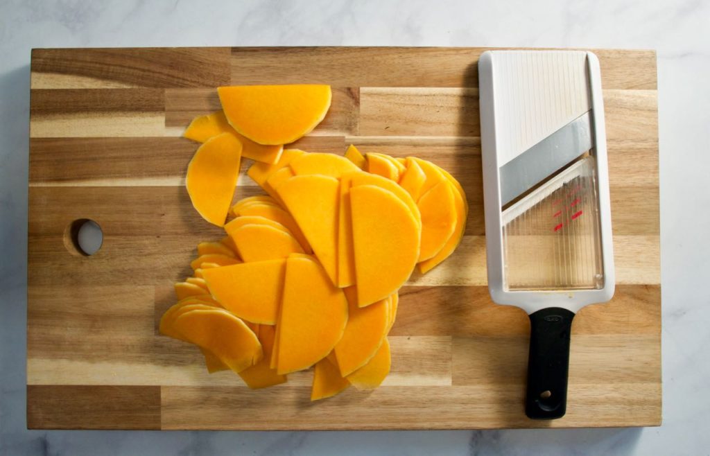 Butternut Squash slices next to mandolin on chopping board.