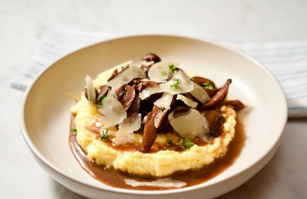 Bowl of polenta topped with mushroom ragout, parmesan shavings and thyme.