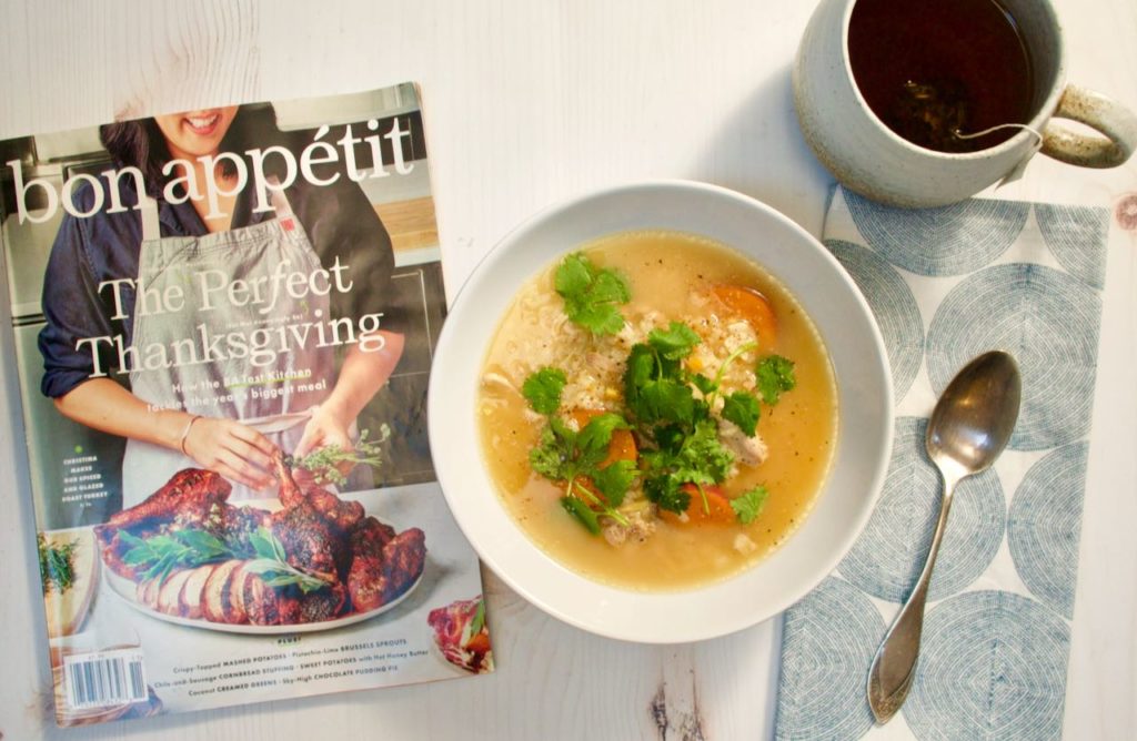 Bowl of soup, Bon Appetit magazine, spoon on napkin and mug with tea.