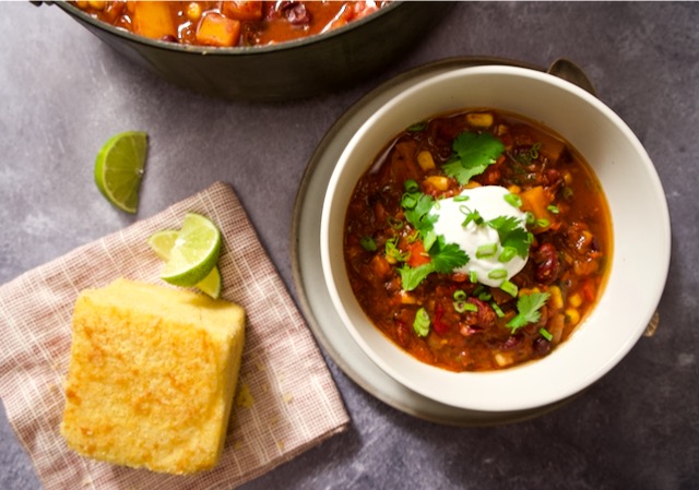 Bowl of butternut squash and bean chili, cornbread on napkin and pot.