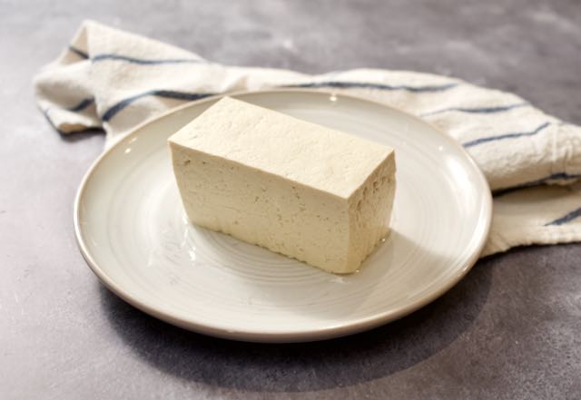 Block of tofu on plate with towel.