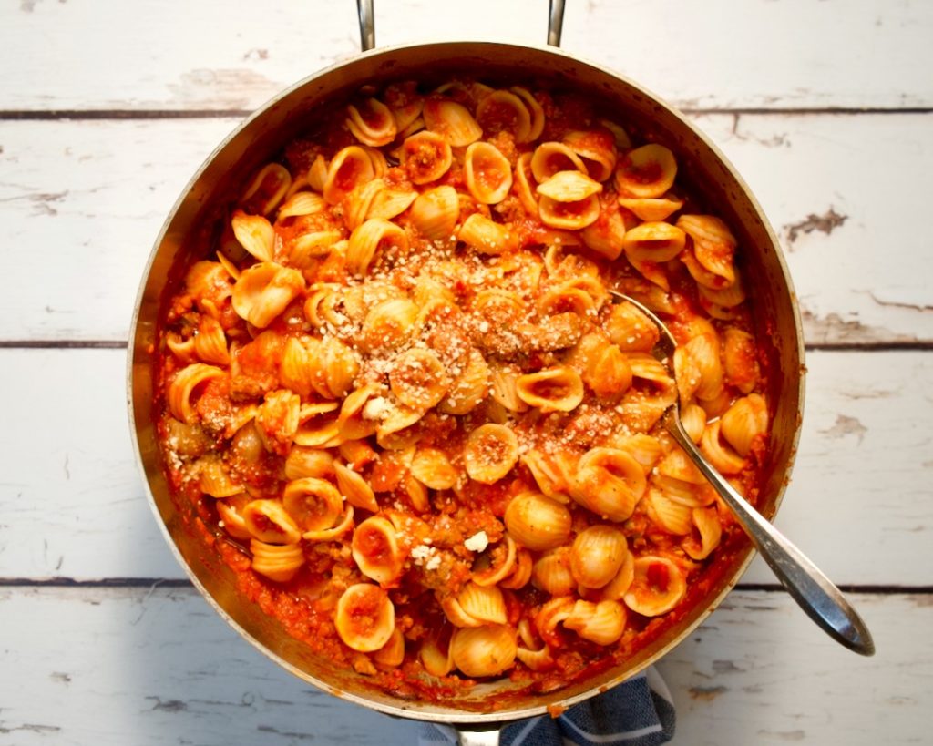 Pasta with ragu in pot with spoon. 