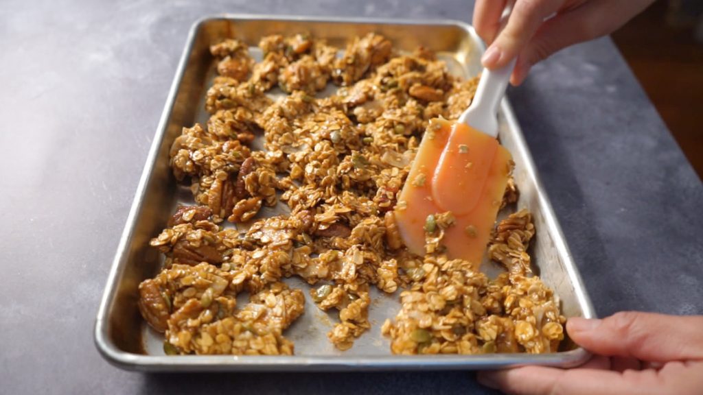 Granola being spread on a baking sheet.