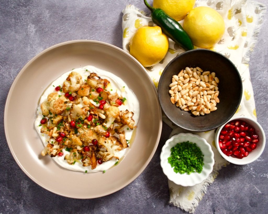 Lemon roasted cauliflower with bowls of garnishes, lemons and peppers.