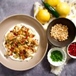Lemon roasted cauliflower in bowl with small bowls of garnishes, lemons and peppers.