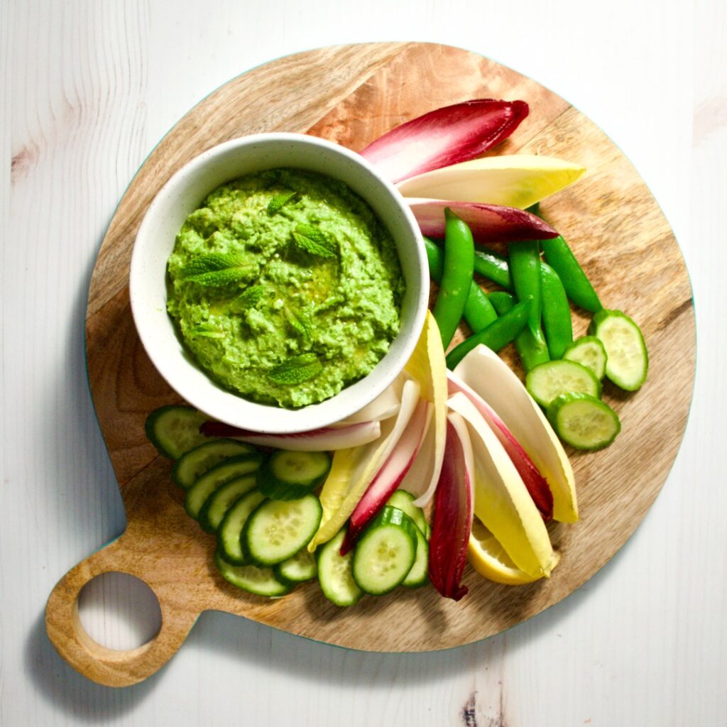 Green pea dip with raw vegetables on a platter.