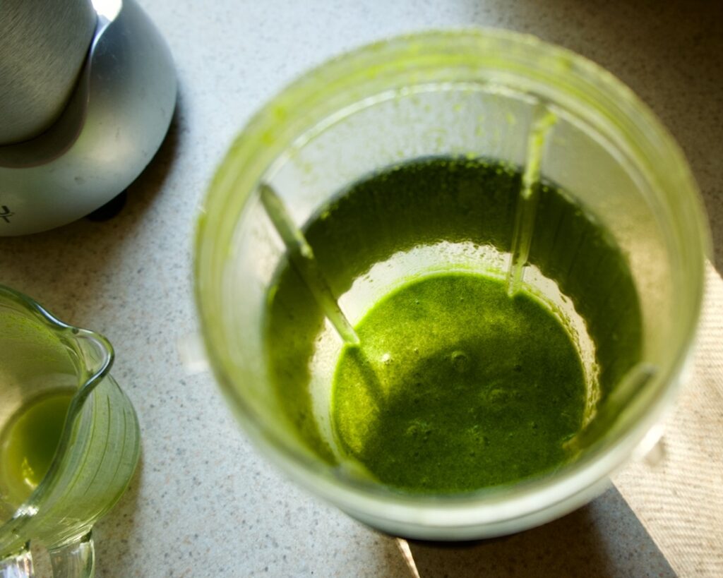 Blended green liquid in blender with measuring cup.