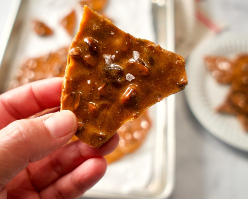 Brittle held in hand. Plate and sheet pan behind.