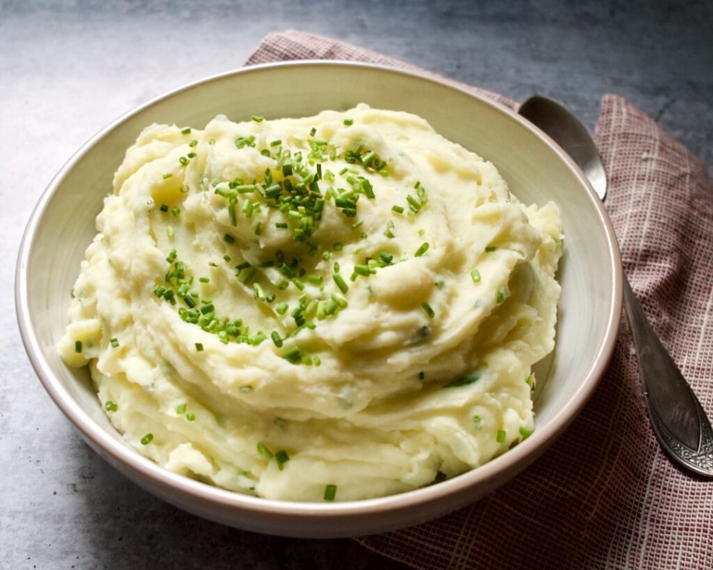 Mashed potatoes in bowl with towel and spoon.