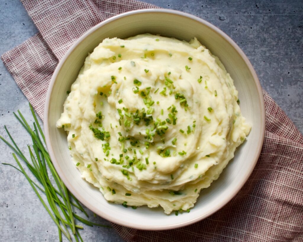 Bowl of mashed potatoes, red towel and chives.
