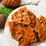 Pistachio brittle on plate with pine cones and pine branches.