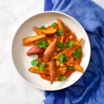 Baked sweet potato wedges in bowl with sauce on blue towel.