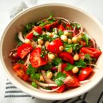 Tomato and chickpea salad in large mixing bowl with towel.