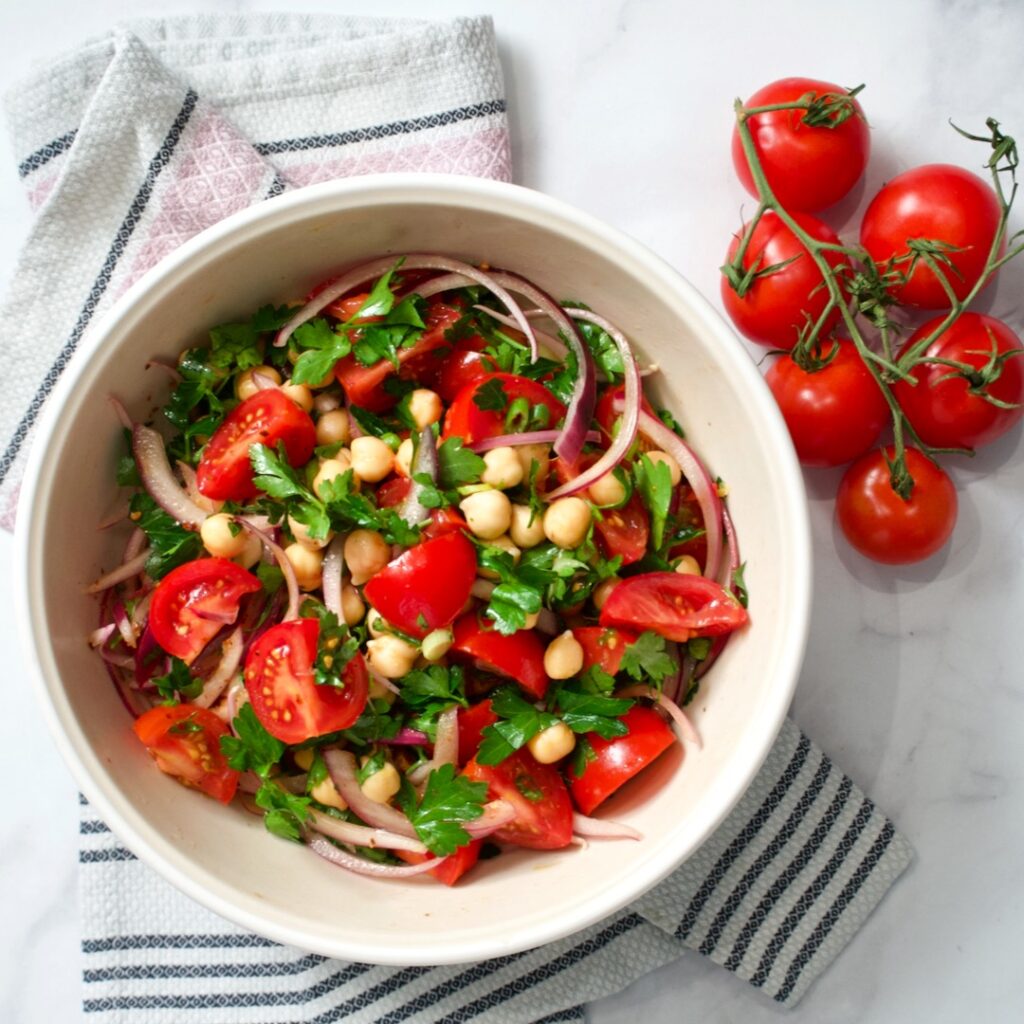 Tomato and chickpea salad in large mixing bowl with towel and vine tomatoes.