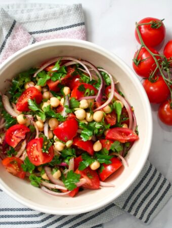 Salad bowl with tomatoes and chickpeas on towel. Vine tomatoes on the side.