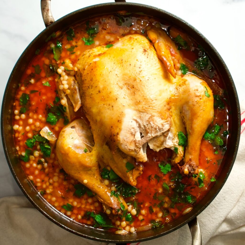 Whole chicken in pot with broth and pasta.