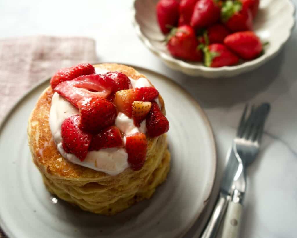 Johnny cakes on a plate with knife and fork and bowl of strawberries.