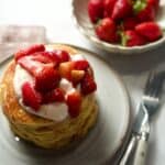 Cornmeal pancakes with strawberries and yogurt. Knife and fork. Bowl of strawberries behind.