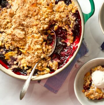 Mixed berry crisp in pan with spoon. Serving in a small bowl with ice cream.