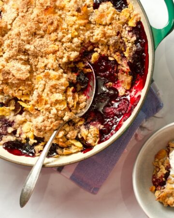 Mixed berry crisp in pan with spoon. Serving in a small bowl with ice cream.