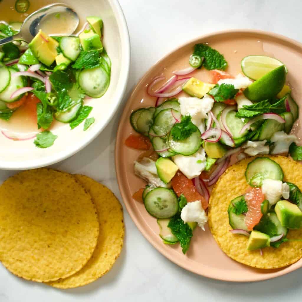 Flaked fish, cucumber salad on a plate and in a bowl with two tostadas. Recipe from Cook This Book by Molly Baz.